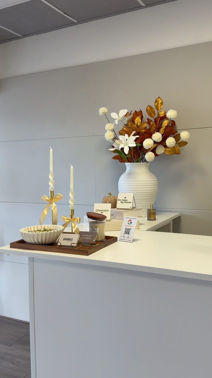 De balie van de salon in herfstsfeer: witte toonbank, het bordje De Salon by Shania, kaarsen met gouden strikken en herfstbloemen