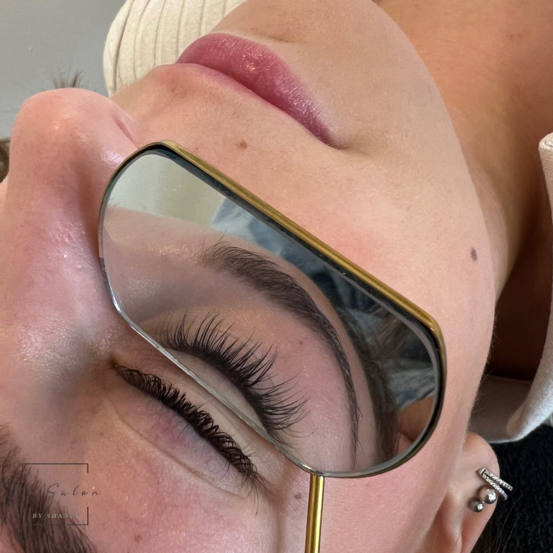 Na een lashlift bekijkt een klant het resultaat in een handspiegel met een gouden rand