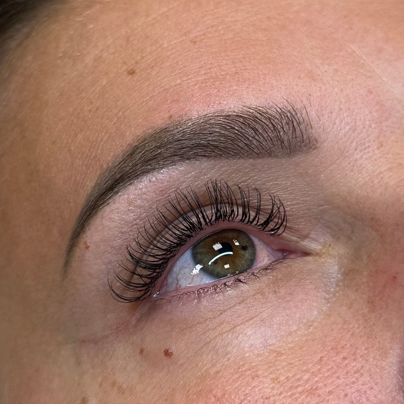 Een set wimperextensions bij een groenbruin oog en een verzorgde wenkbrauw